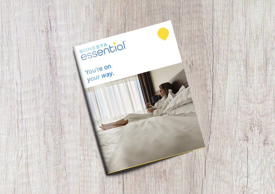 The Sonesta Essential Brand Brochure in front of a gray, wooden background.